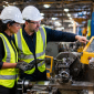 Two factory workers in protective gear discussing safety features on a metal lathe, highlighting machine guarding and operational safety.