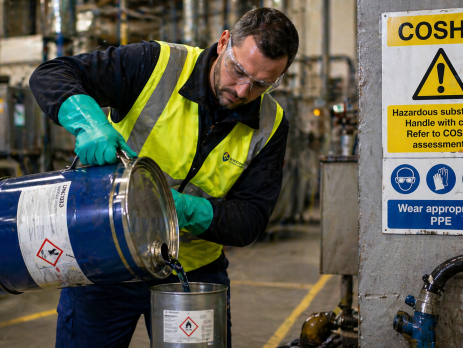 A UK factory worker wearing personal protective equipment handles hazardous substances, demonstrating COSHH compliance in an industrial setting.