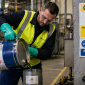 A UK factory worker wearing personal protective equipment handles hazardous substances, demonstrating COSHH compliance in an industrial setting.